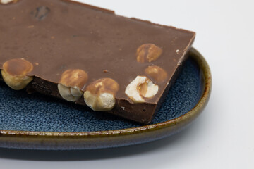 Detailed view of a milk chocolate bar with whole hazelnuts, presented on a decorative blue ceramic plate.