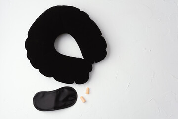 Black neck pillow with sleep mask and earplugs on white background