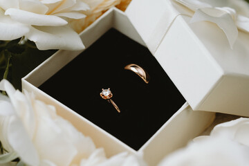 Gold wedding and engagement rings in box surrounded by white roses