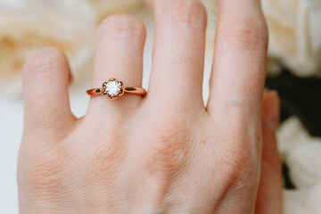 Engagement ring on woman's hand with soft floral background