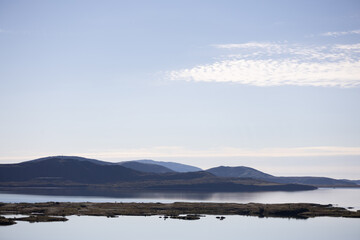 Tranquil lake with distant mountains under clear blue sky, reflecting peaceful natural beauty.