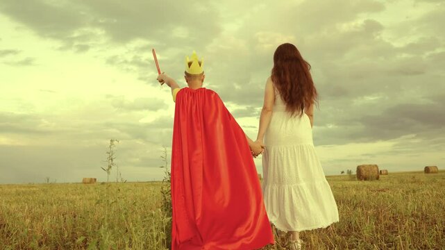 happy family. boy son with mother plays red cape superhero meadow. happy family concept. chidhood dream. golden crown on his head. child dream kid protect help group people. teamwork. fantastic game