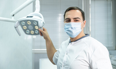 Professional male dentist in mask standing next to dentists chair in dental office. Healthcare and medicine concept 