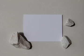 Empty card with white decorated stones and sunlight shadows on neutral background. Aesthetic composition for minimalistic template in flat lay style.