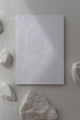 Empty card with white decorated stones and sunlight shadows on neutral background. Aesthetic composition for minimalistic template in flat lay style.
