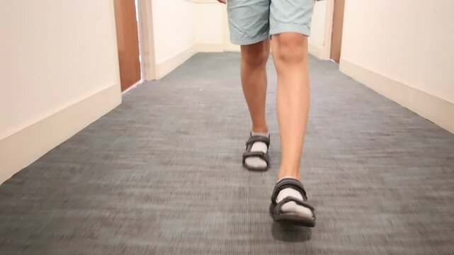 young man walking down a carpeted hallway wearing sandals camera moves backward in front of him capturing each step in slow steady motion indoor casual scene