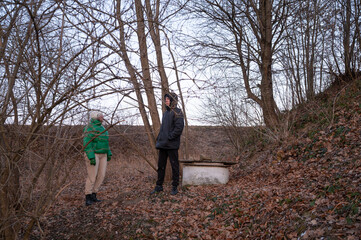 As dusk settles over the tranquil forest, two friends wander through the peaceful, wooded area, exchanging tales and laughter while the leaves gently fall around them