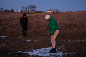 Evening exploration in early winter light reveals two figures in a quiet rural setting engaged in a curious moment by the frost covered ground