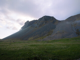 Grey rocky mountains in Iceland. Mountain peaks on a cloudy day with grass at the foot.