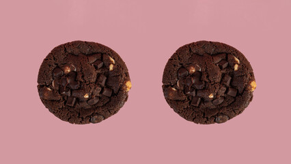 A large chocolate cookie topped with chocolate chips on a pink background
