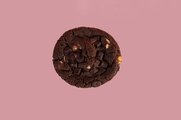 A large chocolate cookie topped with chocolate chips on a pink background