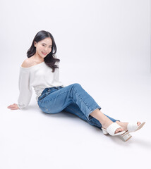 Portrait happy smile young asian beautiful woman curly hair wearing long sleeved shirt, blue jeans outfit, casual relax on floor in studio, sitting on white background joy positivity fashion concept.