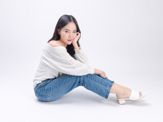Portrait happy smile young asian beautiful woman curly hair wearing long sleeved shirt, blue jeans outfit, casual relax on floor in studio, sitting on white background joy positivity fashion concept.