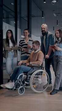 A businessman with disability in a wheelchair is surrounded by supportive colleagues in a modern office, showcasing the strength of teamwork, inclusivity, and empowerment in the face of challenges. 
