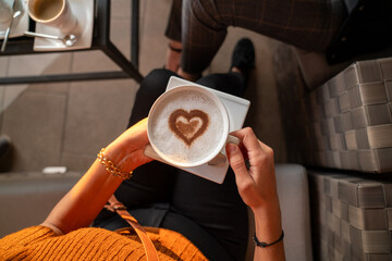 A woman holding a cup of heart shaped coffee latte .