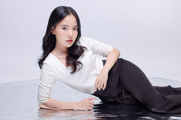 Portrait cheerful young asian beautiful woman curly hair wearing long sleeved shirt, black long pants outfit casual relax on floor in studio laydown on white background joy positivity fashion concept