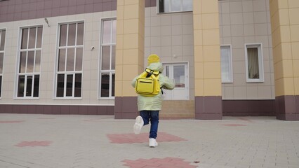 small child with backpack rushes to school for lesson, kid with school bag on his shoulders runs to...