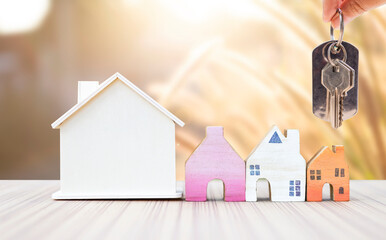 House key in girl hand with miniature wooden house model over blurred nature background, property and real estate business concept