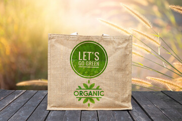 Jute bag with green logo on wooden foor over blurred nature background, environmental friendly product concept