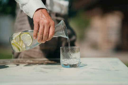 Man pours lemon water into glass on table for healthy refreshment and detox