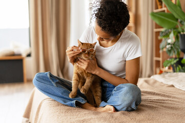Young woman putting glasses on ginger cat while sitting on bed