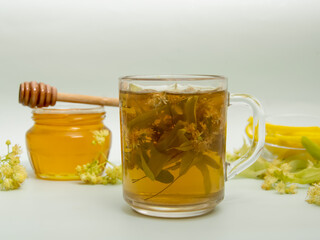 A cup of lime tea with leaves, flowers and a jar of honey on a light background 