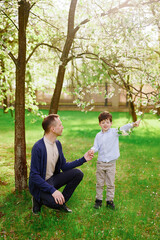 father and son exploring nature together in spring park, bonding over blooming trees. young boy holding flowering branch, enjoying sunny day outdoors, wearing casual attire.
