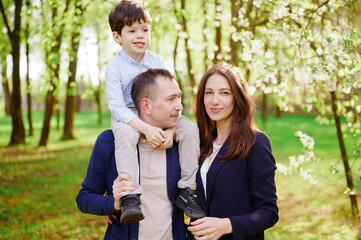 happy family enjoying spring day outdoors. father with son on shoulders, mother smiling near...