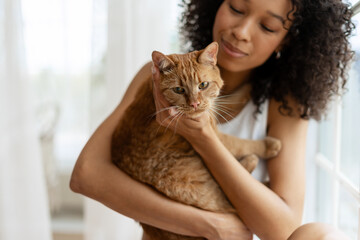 Young woman holding ginger cat with love and care