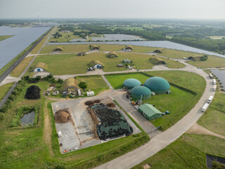 Aerial view of renewable energy site with biogas domes, combined heat and power station, solar fields, silage storage, repurposed munitions depot as sustainable infrastructure in rural landscape.