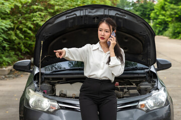 Asian woman using phone calling car mechanic to fix broken car on road