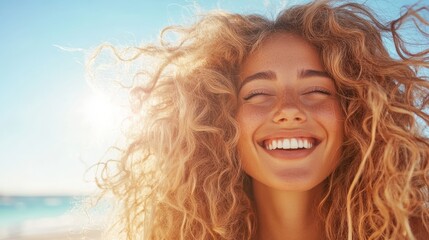 A joyful young woman with curly hair smiles radiantly at the beach, capturing the essence of happiness and carefree summer vibes against a sunny backdrop.