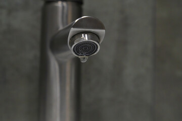 Close-up of a dripping faucet wasting water, highlighting the importance of water conservation and plumbing maintenance with a blurred background