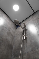 Modern shower head hanging elegantly in a contemporary bathroom, highlighting its sleek design and functionality against a stylish backdrop of gray tiles, enhancing the space's luxury and comfort