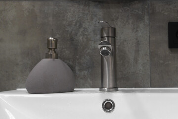 Featuring a sleek, modern faucet and stylish soap dispenser atop a clean white sink, enhancing the minimalist aesthetic against a textured gray tiled wall