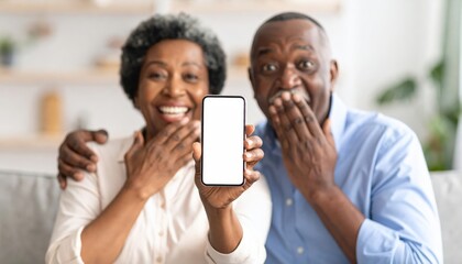 Happy couple showing smartphone with excitement while sitting together in a cozy living room, expressing joy and surprise