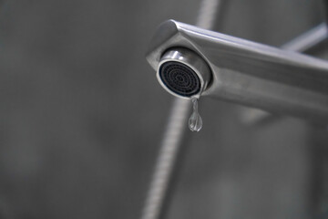 Close-up view of a dripping faucet in a modern bathroom, emphasizing water waste and underscoring the urgent need for repair or replacement to prevent resource loss