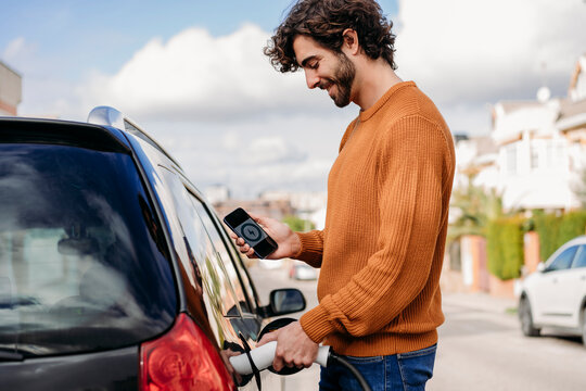 Smiling young man charging car at electric vehicle charging station