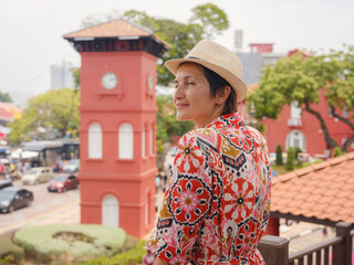 Young woman in ethnic dress and hat exploring the vibrant streets of Malacca, Malaysia. A blend of...
