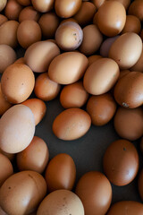 A close-up of a pile of brown chicken eggs with natural imperfections and earthy tones, freshly collected and displayed for sale at a traditional local market stall.