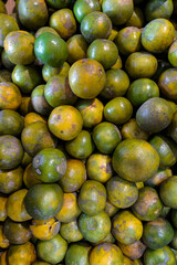 A full frame of fresh green-yellow oranges with natural blemishes and varied textures, stacked together at a traditional market, ready to be sold as local tropical fruit.