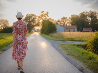 Young woman walking through picturesque European field in late summer. Golden sunlight, lush...