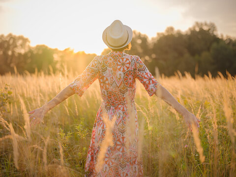 Young woman walking through picturesque European field in late summer. Golden sunlight, lush greenery, and serene rural atmosphere create peaceful countryside scene.