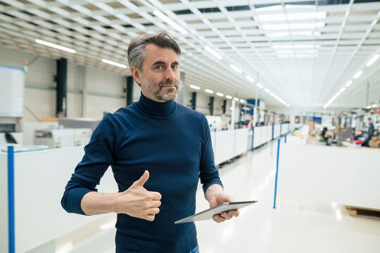 Smiling businessman with tablet PC showing thumbs up gesture in industry