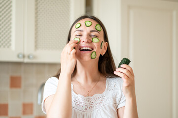 Woman with cucumber slices on her face enjoying a healthy skincare routine in a bright kitchen