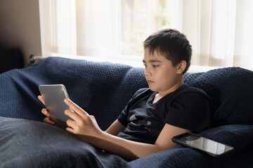 Young boy sitting on sofa using tablet computer at home,Kid leisure in casual digital lifestyle, screen time or online learning,Concept modern childhood and technology Education for Back to school