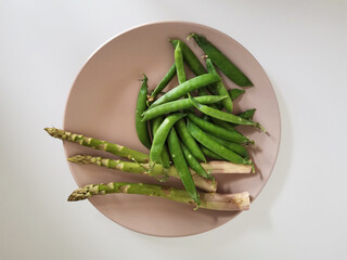 Heap of fresh peas and asparagus on a beige plate isolated on white background from a high angle view