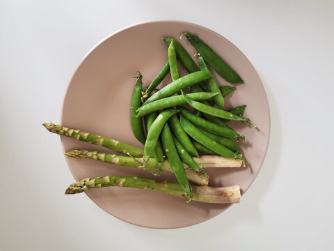Heap of fresh peas and asparagus on a beige plate isolated on white background from a high angle view