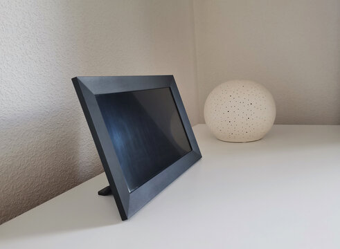 Black digital photo frame mockup with a copy space on white countertop with decorative spherical lamp