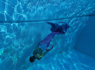 Young woman with mermaid tail swims and dives under sunlit deep water